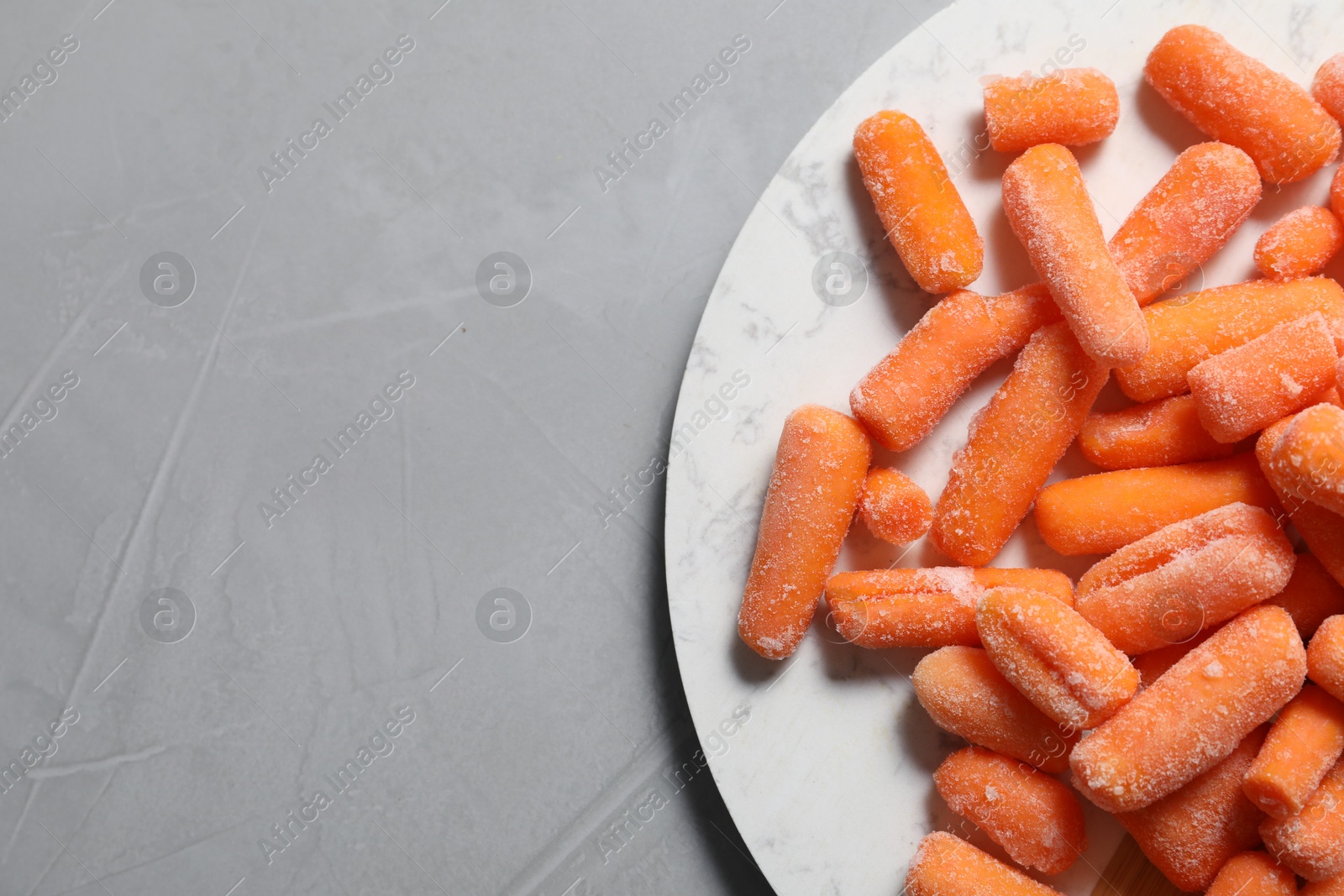 Photo of Frozen baby carrots on grey table, top view. Space for text