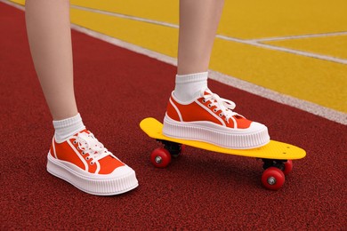 Woman with yellow penny board wearing classic old school sneakers on sport court outdoors, closeup