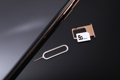 5G SIM card, smartphone and ejector on black background, above view