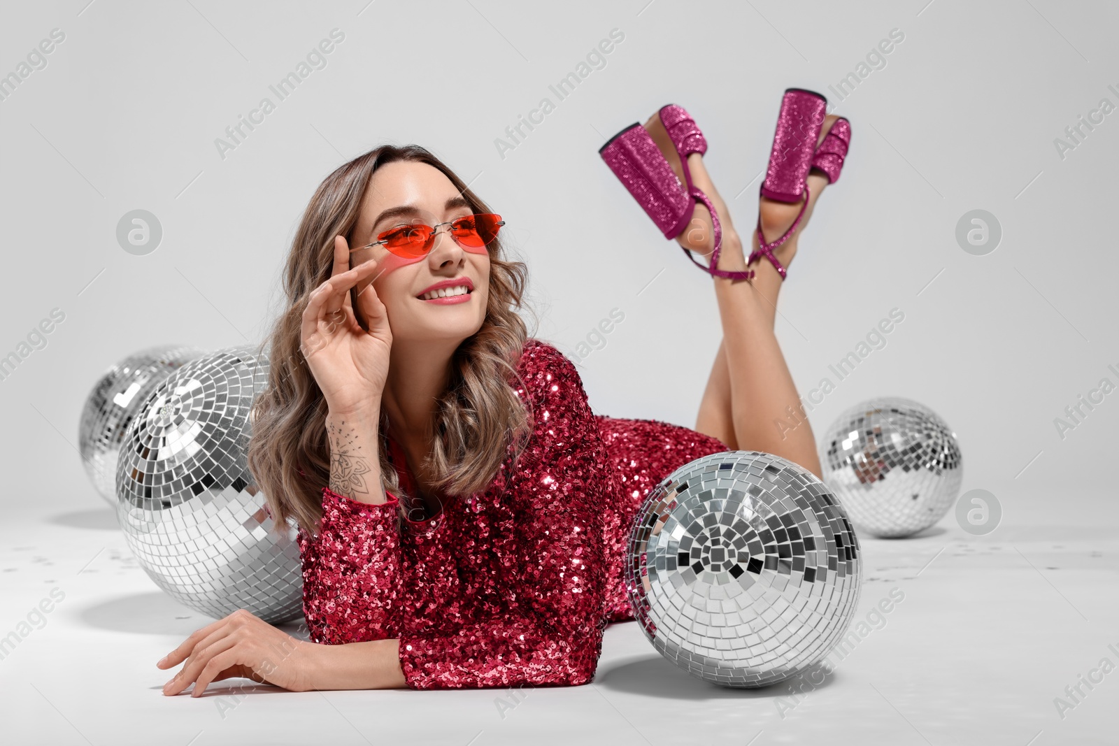 Image of Beautiful woman in sunglasses and sequin dress among disco balls on white background