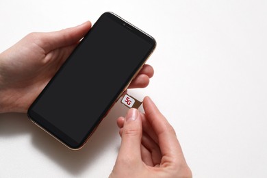 Woman putting slot tray with 5G SIM card in smartphone at white table, closeup