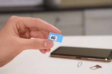 Woman with 6G SIM card at white table indoors, closeup