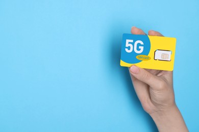 Woman holding 5G SIM card on light blue background, closeup. Space for text