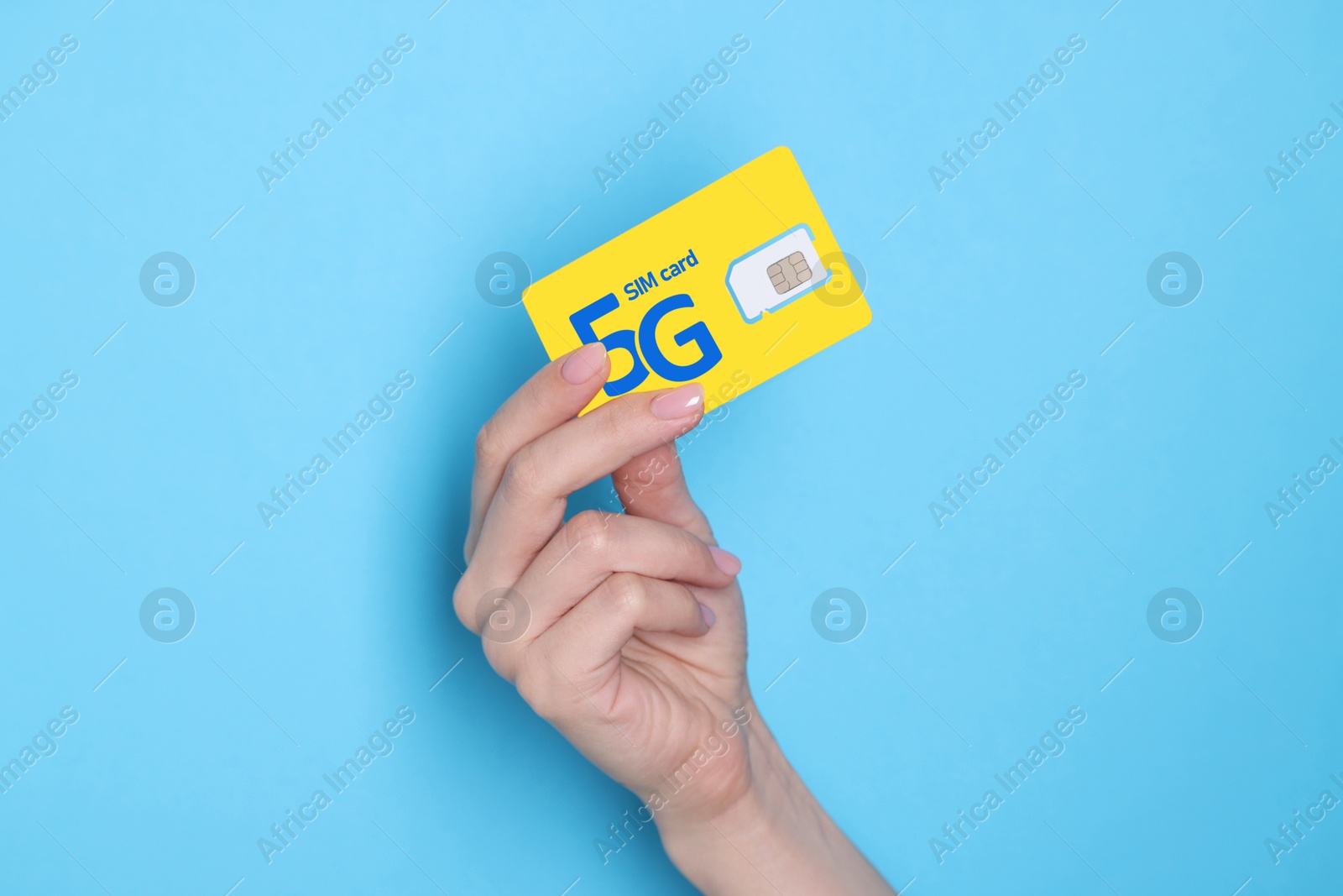 Image of Woman holding 5G SIM card on light blue background, closeup