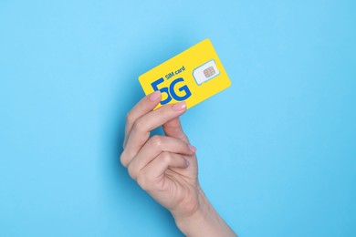 Woman holding 5G SIM card on light blue background, closeup