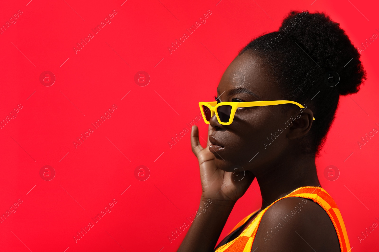 Image of Fashionable portrait of beautiful woman with stylish yellow sunglasses on red background, space for text