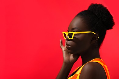 Image of Fashionable portrait of beautiful woman with stylish yellow sunglasses on red background, space for text