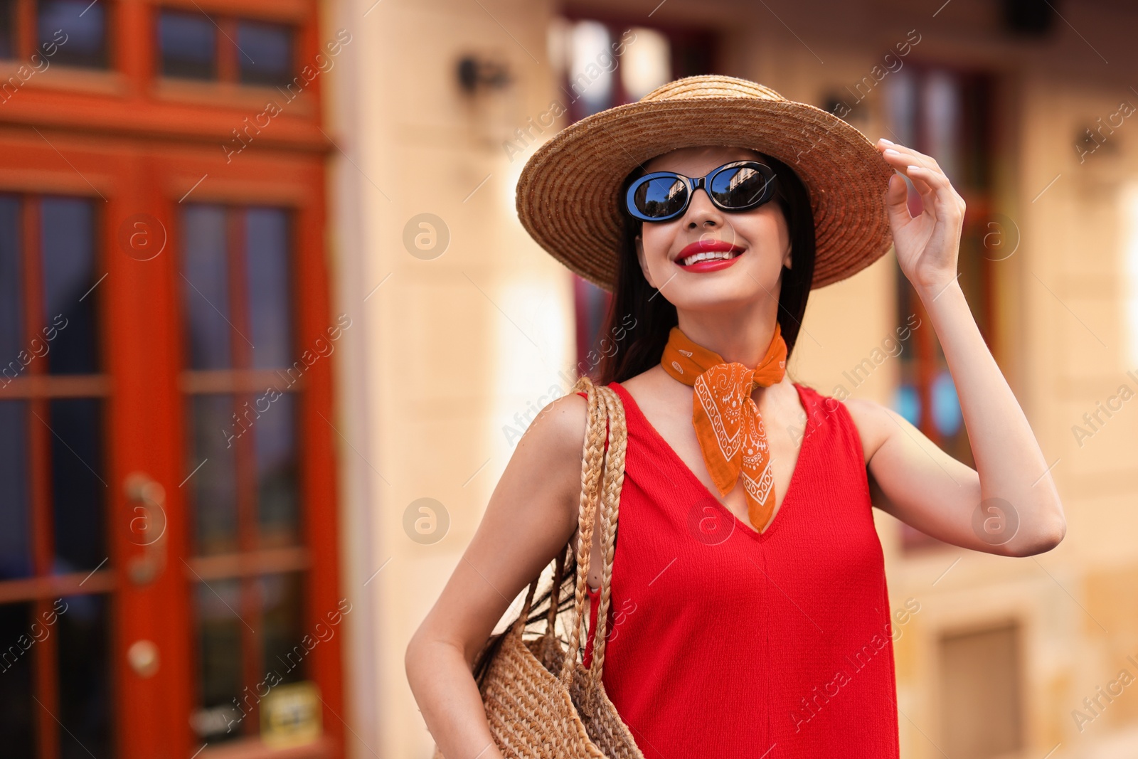 Image of Smiling young woman in stylish hat and sunglasses on city street