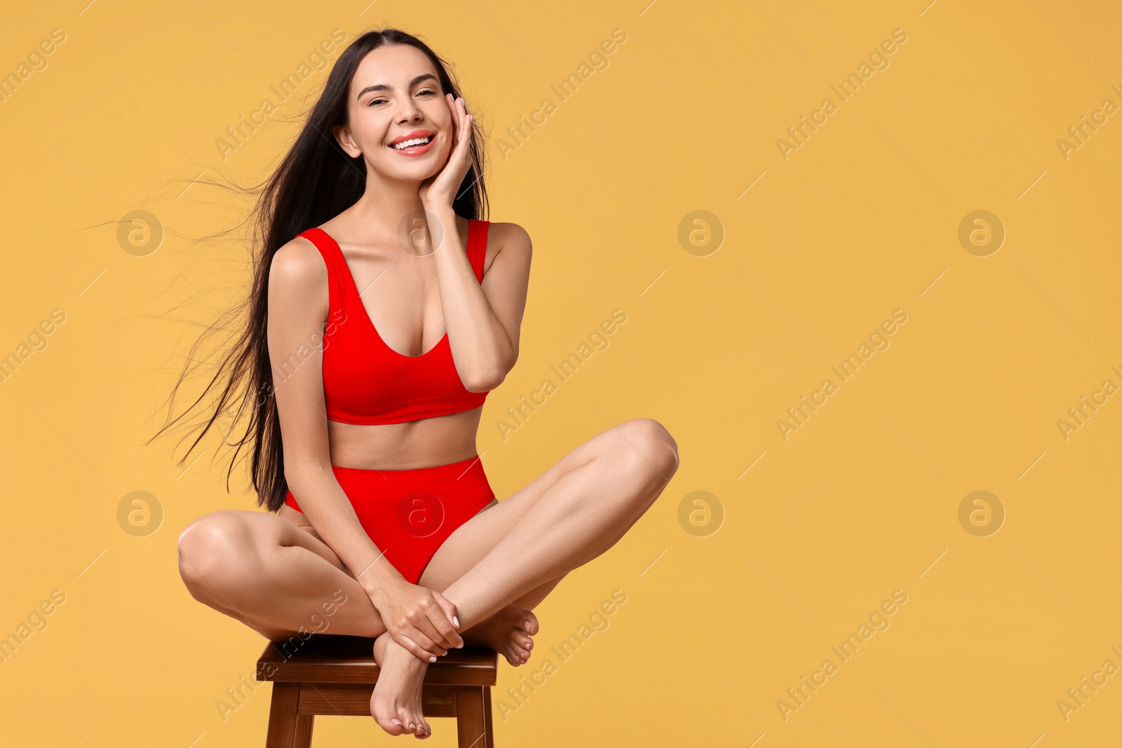 Image of Smiling woman with perfect skin in underwear posing on stool against golden background, space for text. Body care