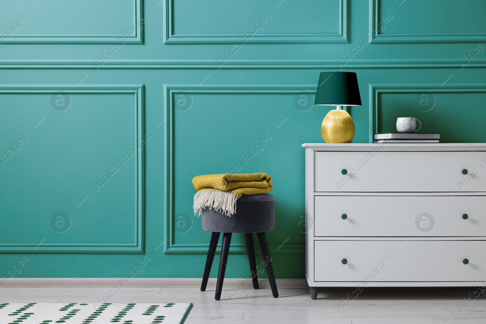 Image of Stylish interior. Stool and chest of drawers near light teal wall, space for text