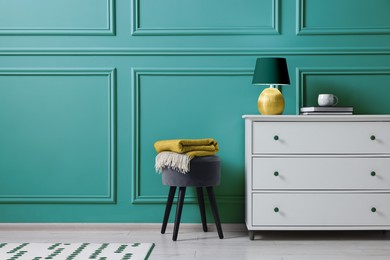 Stylish interior. Stool and chest of drawers near light teal wall, space for text