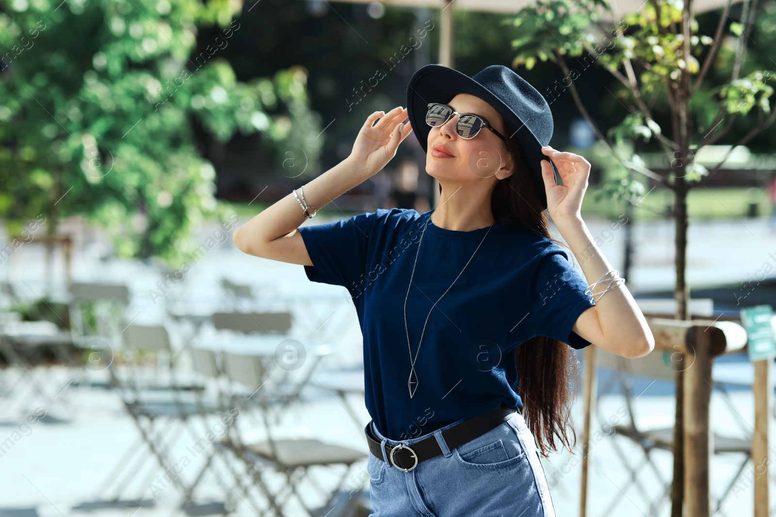 Image of Young woman in stylish black hat and sunglasses on city street