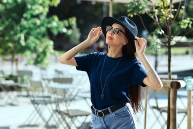 Image of Young woman in stylish black hat and sunglasses on city street