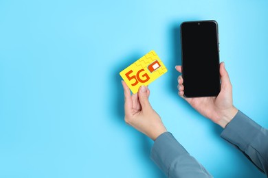 Image of Woman holding 5G SIM card and smartphone on light blue background, closeup. Space for text