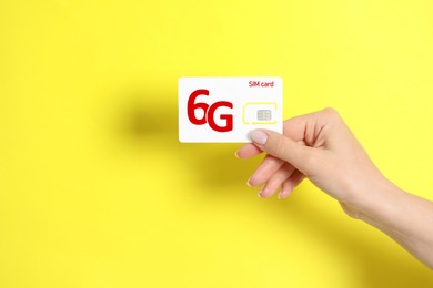 Woman holding 6G SIM card on yellow background, closeup. Space for text