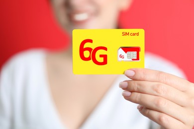 Woman holding 6G SIM card on red background, closeup