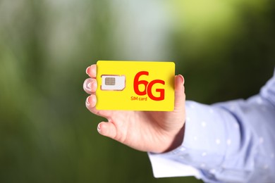 Woman holding 6G SIM card on blurred background, closeup