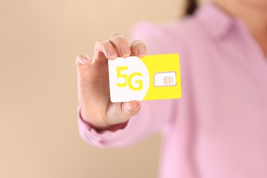 Woman holding 5G SIM card on beige background, closeup