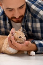 Man petting cute ginger cat on floor at home