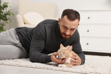 Photo of Man petting cute ginger cat on floor at home