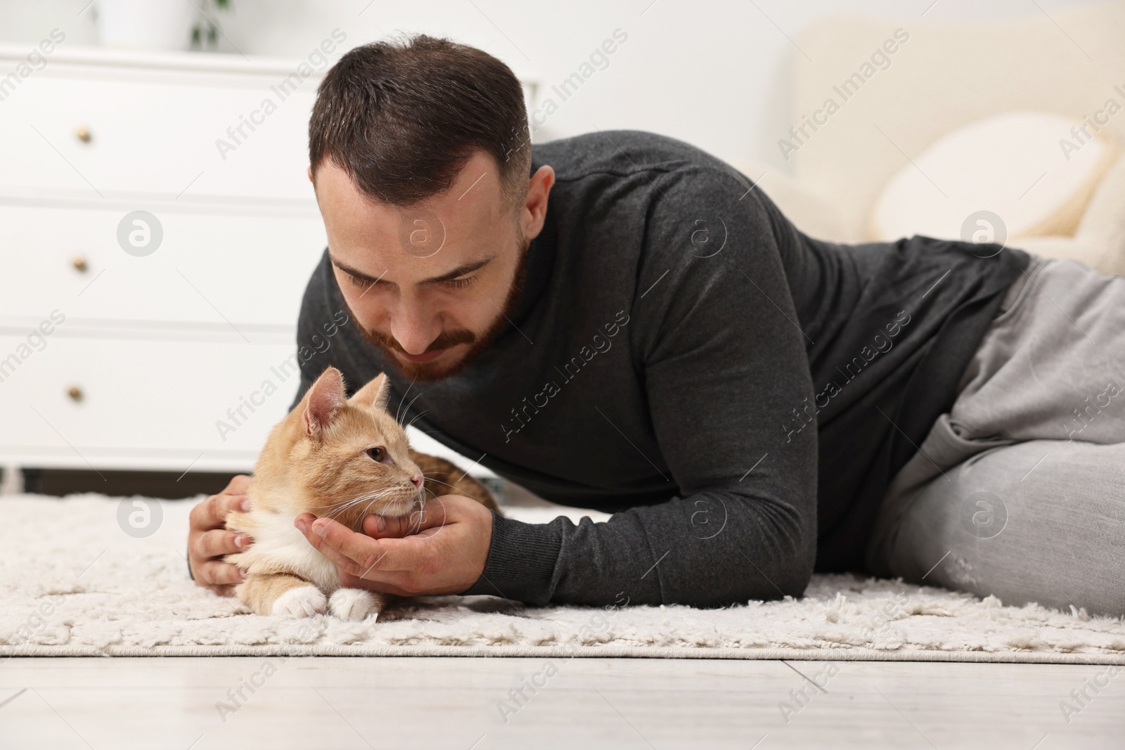 Photo of Man petting cute ginger cat on floor at home