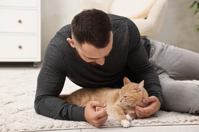 Photo of Man petting cute ginger cat on floor at home