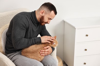 Man petting cute ginger cat on armchair at home