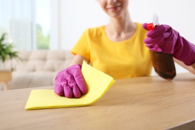 Woman cleaning table with rag and spray at home, closeup