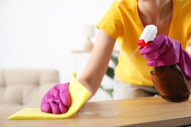 Woman cleaning table with rag and spray at home, closeup