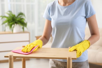 Young woman cleaning wooden shelf with rag at home, closeup