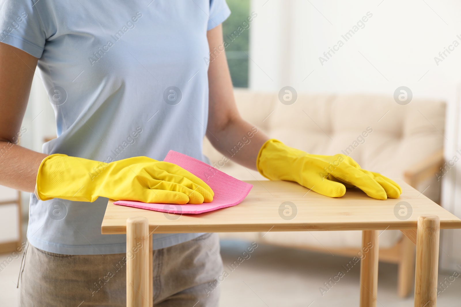 Photo of Young woman cleaning wooden shelf with rag at home, closeup