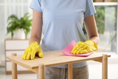 Young woman cleaning wooden shelf with rag at home, closeup