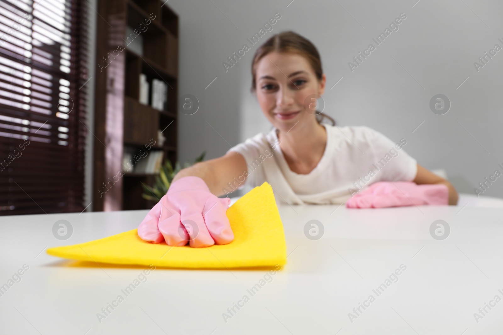 Photo of Young woman cleaning table with rag and spray in office