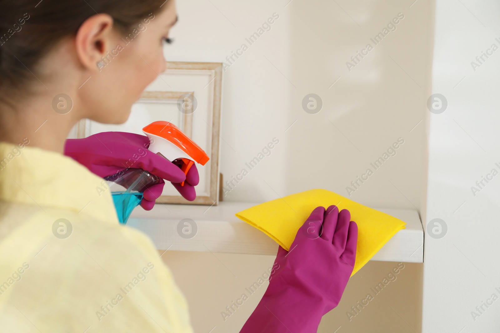 Photo of Young woman cleaning shelf with rag and spray at home, closeup