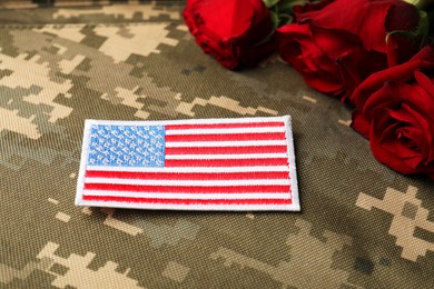 Photo of Veterans day. USA army patch and rose flowers on camouflage fabric, closeup