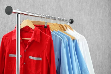 Photo of Different medical workers' uniforms on clothing rack against grey background