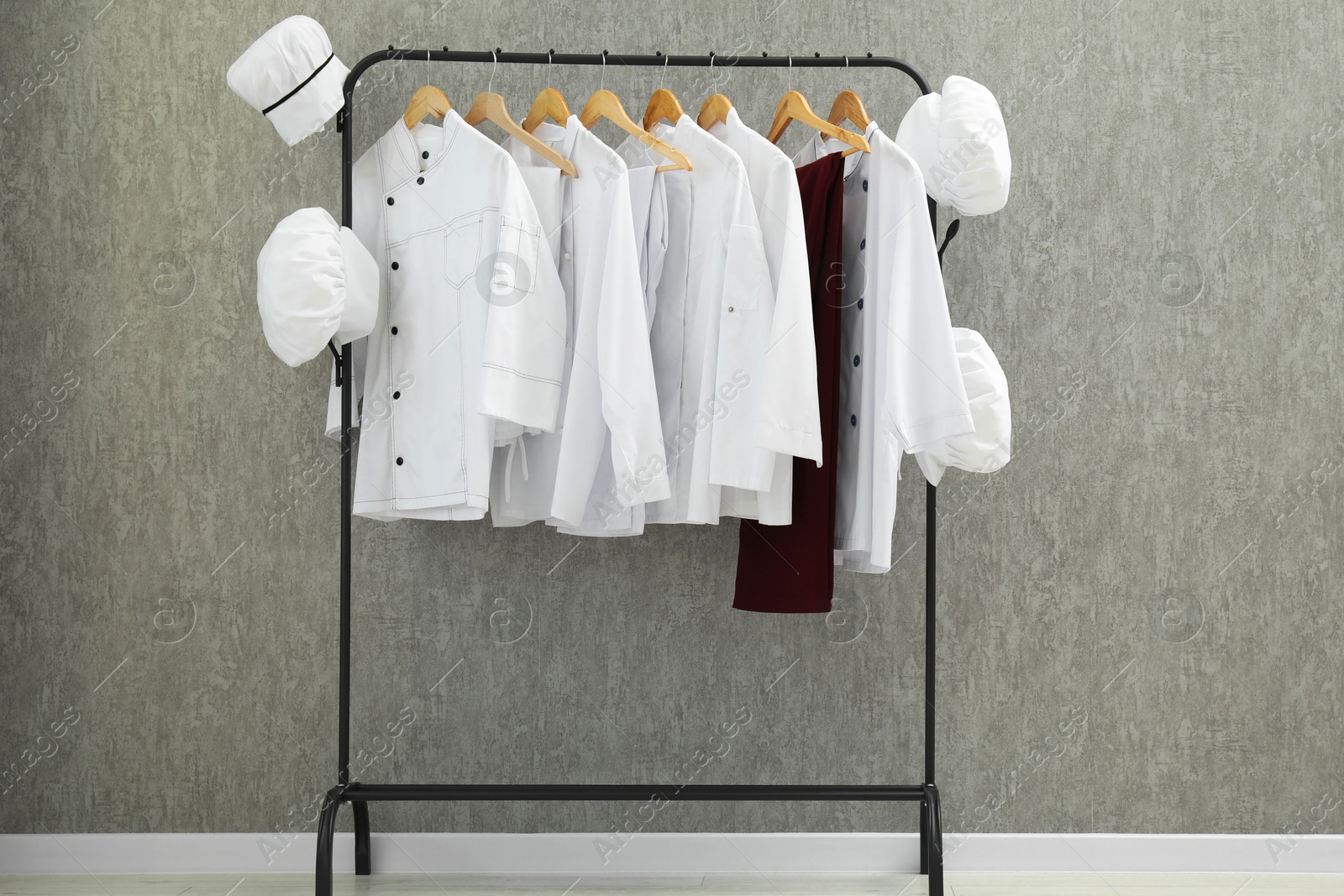 Photo of Chefs' uniforms on clothing rack near grey wall indoors