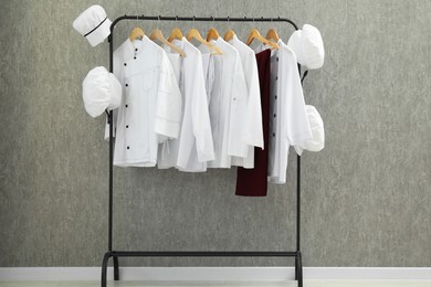 Photo of Chefs' uniforms on clothing rack near grey wall indoors