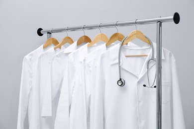 Photo of Different medical workers' uniforms and stethoscope on clothing rack against grey background