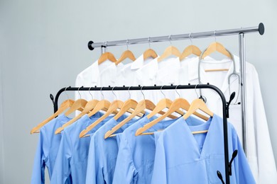 Photo of Different medical workers' uniforms on clothing racks against grey background