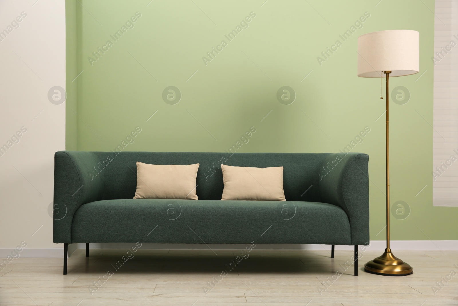 Photo of Stylish sofa with pillows and lamp near green wall indoors