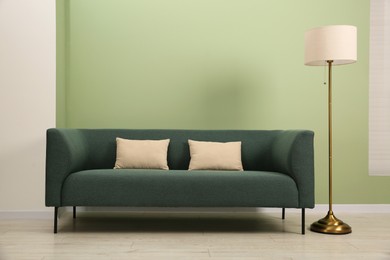 Photo of Stylish sofa with pillows and lamp near green wall indoors