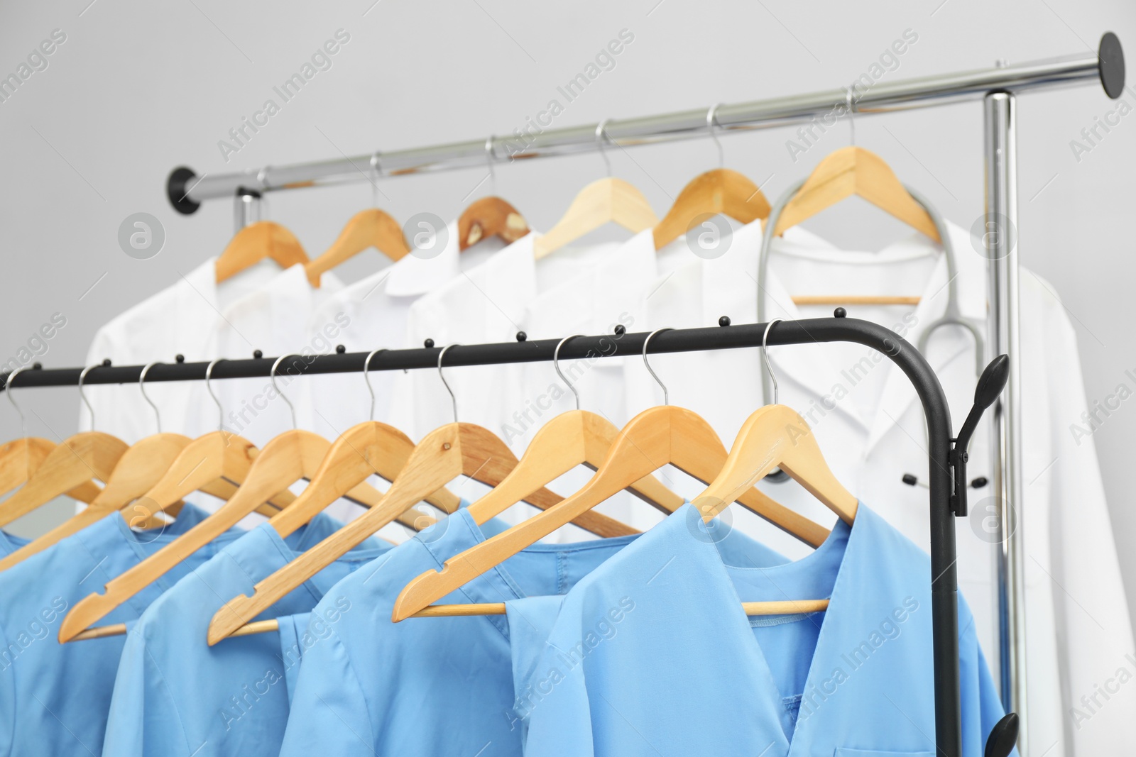 Photo of Different medical workers' uniforms on clothing racks against grey background, closeup