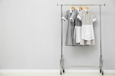 Photo of Maids' uniforms on clothing rack near grey wall indoors. Space for text