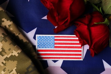 Photo of Veterans day. USA army patch, rose flowers and military uniform on American flag, flat lay