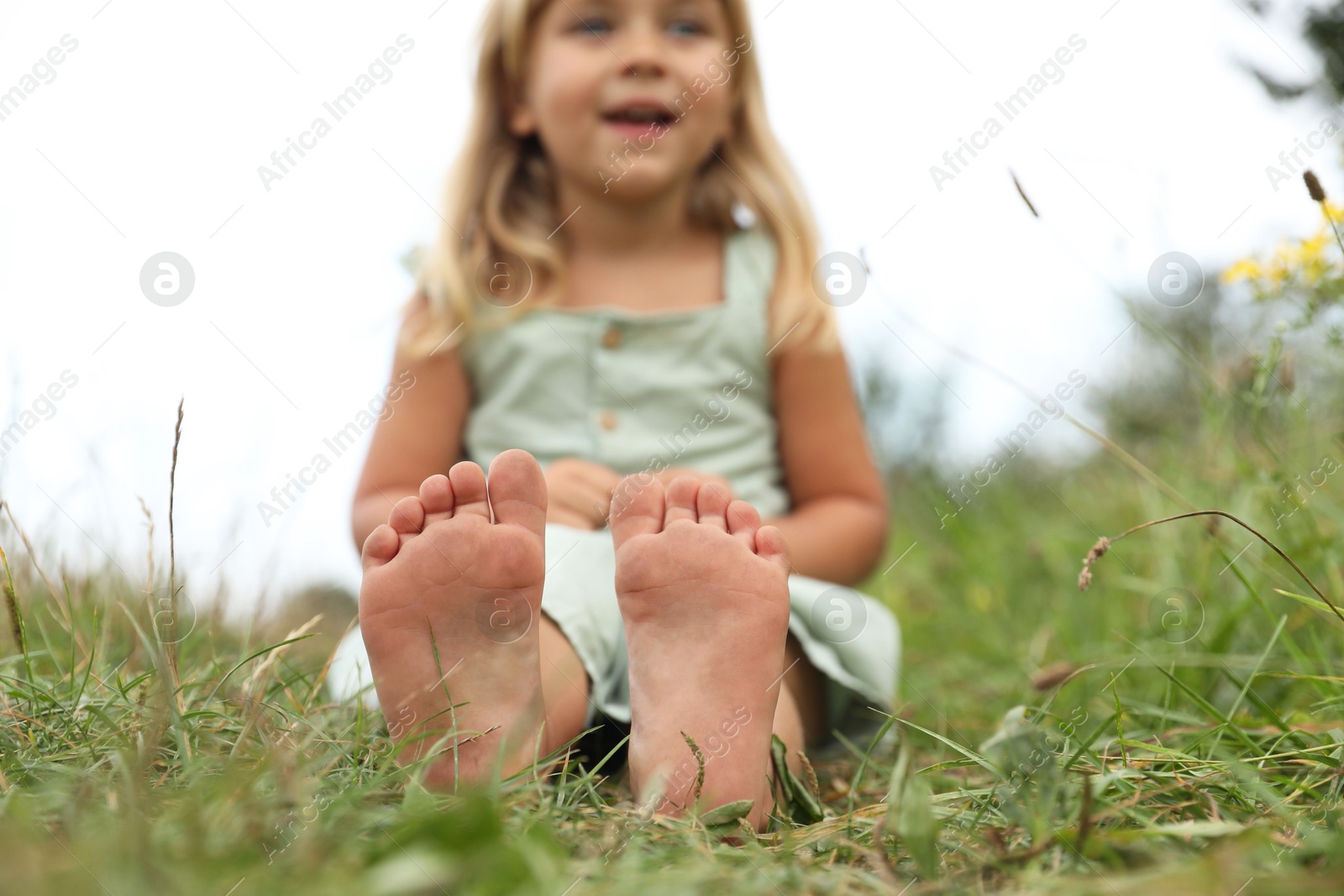 Photo of Barefoot little girl on green grass at meadow, selective focus. Child enjoying beautiful nature