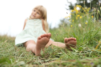 Photo of Barefoot little girl on green grass at meadow, selective focus. Child enjoying beautiful nature