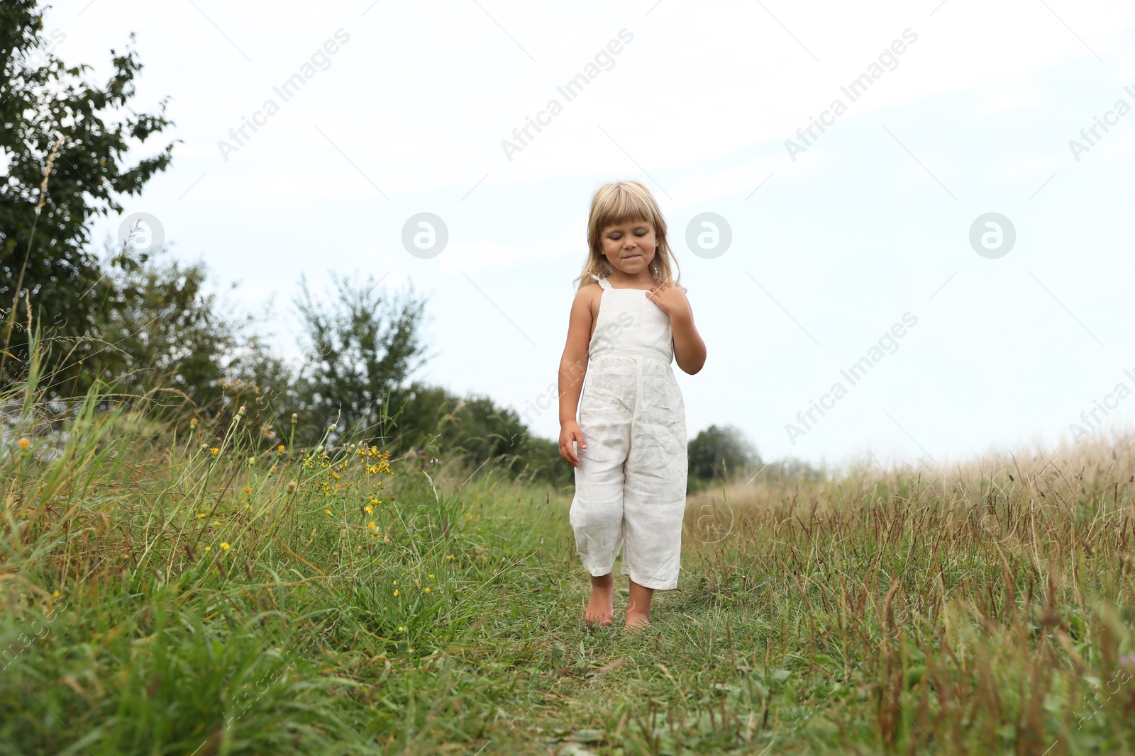 Photo of Cute little girl walking barefoot at meadow. Child enjoying beautiful nature