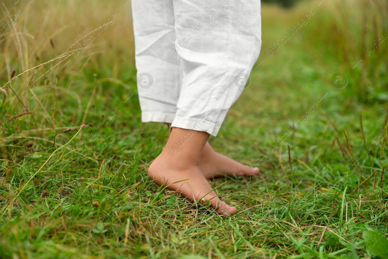 Photo of Little child standing barefoot on green grass outdoors, closeup. Enjoying nature