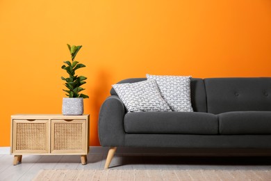 Photo of Stylish sofa with cushions and plant on side table near orange wall